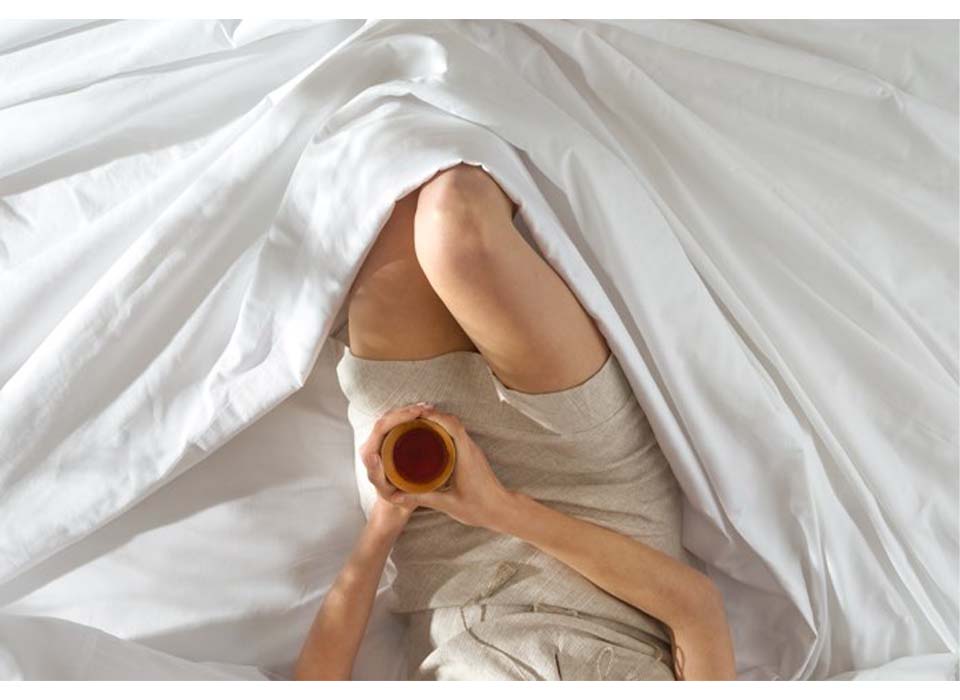 航拍的女人喝咖啡在床上配备的Saatva床单